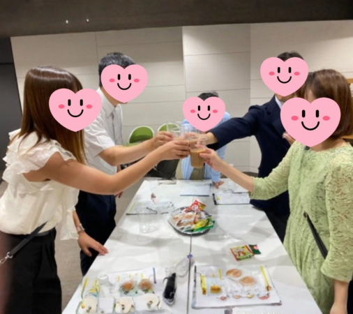 複数の人々がテーブルを囲み、飲み物を手に乾杯をしている様子