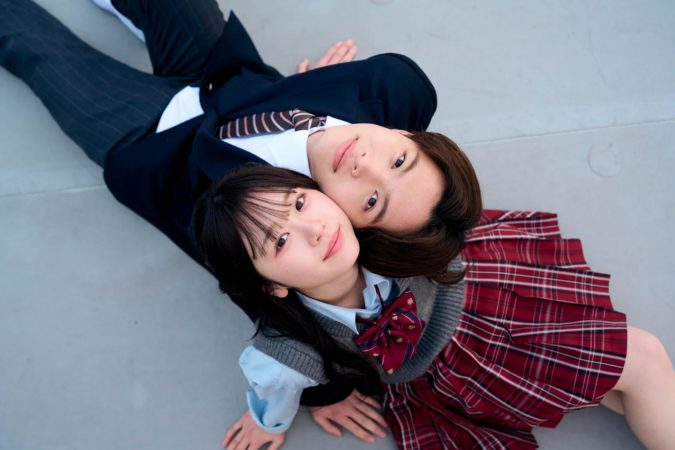 制服姿の若い男女が寄り添い、地面に寝転がってカメラを見上げているポートポートレート写真