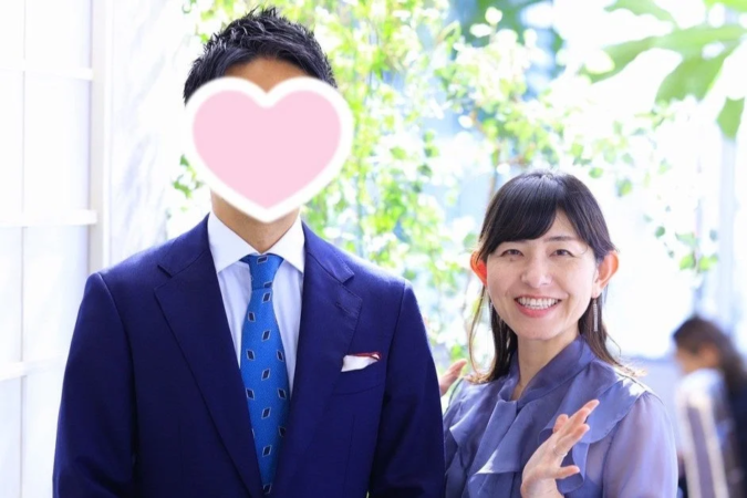 青いスーツ姿の男性(顔はハートで隠されている)と、笑顔でカメラを見つめる紫色のブラウスを着た女性のツーショット