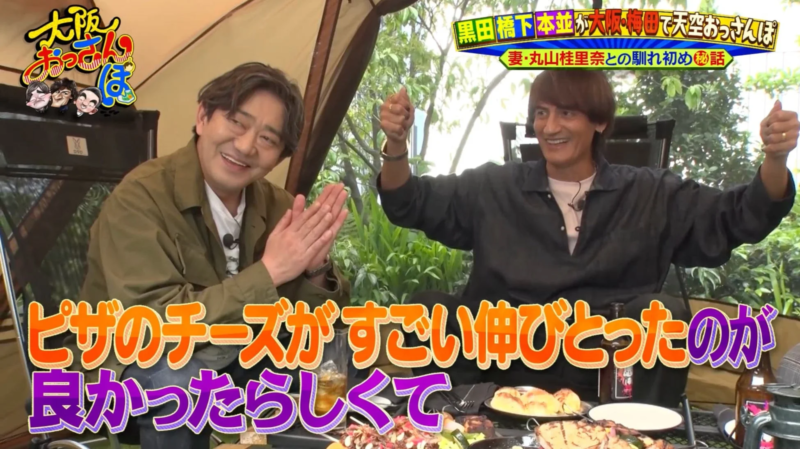 「大阪おっさんぽ」という番組のロケで、二人の男性タレントが屋外で食事をしながら笑顔でトークしている様子。ピザのチーズがよく伸びて美味しかったというテロップが表示されており、和やかな雰囲気が伝わります。
