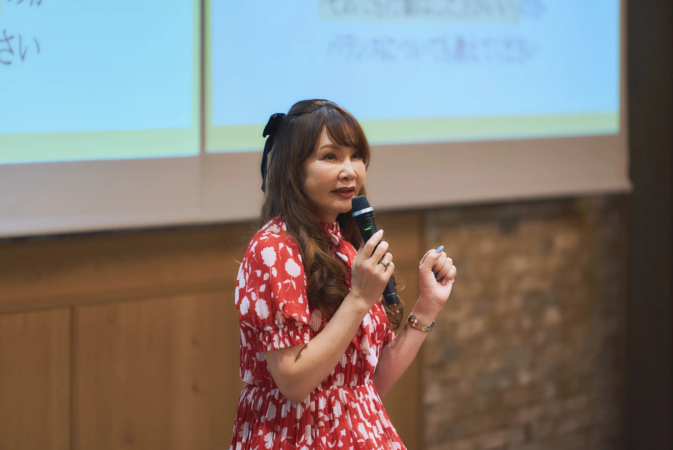 赤いドレスの女性がマイクを持って講演