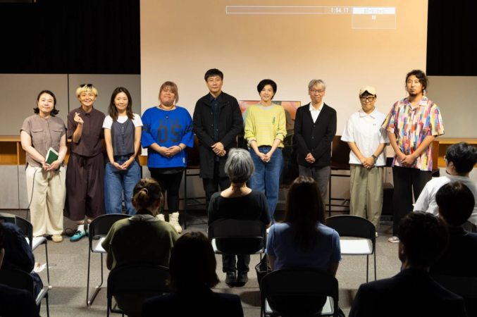 ステージ上に9人の男女が並び、その前に観客が着席しているイベントの様子
