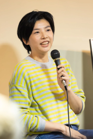 ショートヘアのアジア人女性がマイクを持ち、笑顔で話している