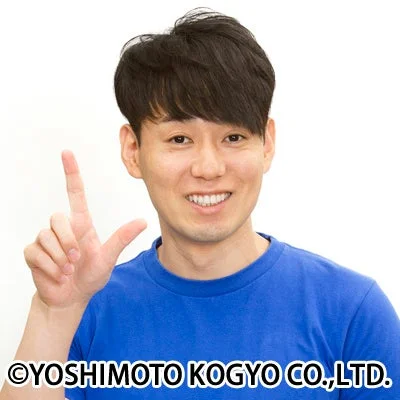 青いTシャツを着たアジア人男性が笑顔でカメラ目線で、左手の人差し指と中指を立ててポーズをとっている