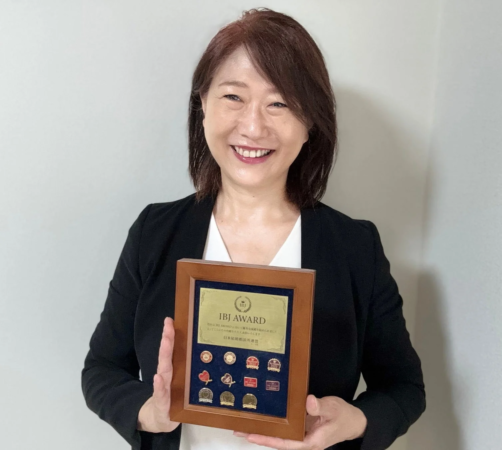 笑顔の女性がIBJ AWARDの表彰状を持つ