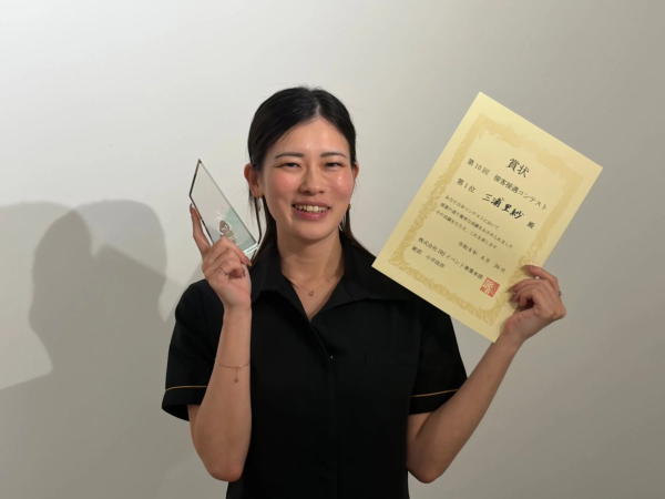「第10回 接客接遇コンテスト」で第1位を獲得し、賞状とトロフィーを手に笑顔で立つ女性