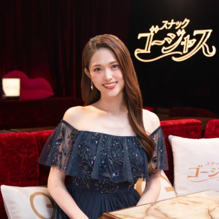 豪華なセットの中で、ネイビーのオフショルダードレスを着た女性が笑顔で座っています。