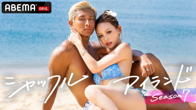 青い海と白い砂浜を背景に、水着姿の男女が密着してポーズをとっている。